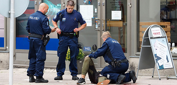 TOPSHOT - Police officers stand next to a person lying on the pavement in the Finnish city of Turku where several people were stabbed on August 18, 2017. Several people were stabbed in the southwestern Finnish city of Turku, police said after shooting and arresting a suspect. Public television station Yle reported that central Turku was on lockdown, with witnesses saying they had seen bodies lying on the ground in a busy area of the town. Businesses were shut. / AFP PHOTO / Kirsi Kanerva