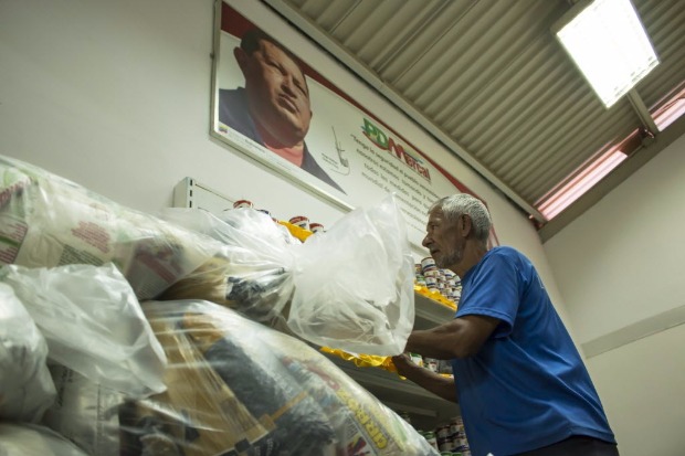 Beneficirio recolhe cesta bsica dos Clap em centro de distribuio com foto de Hugo Chvez