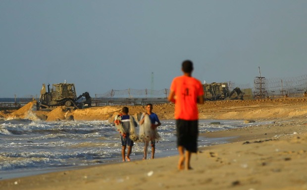 Palestinos andam por praia em Gaza enquanto mquinas trabalham na construo do muro de Israel
