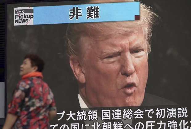 Mulher passa por tela de televisão em Tóquio passando reportagem sobre o discurso de Trump