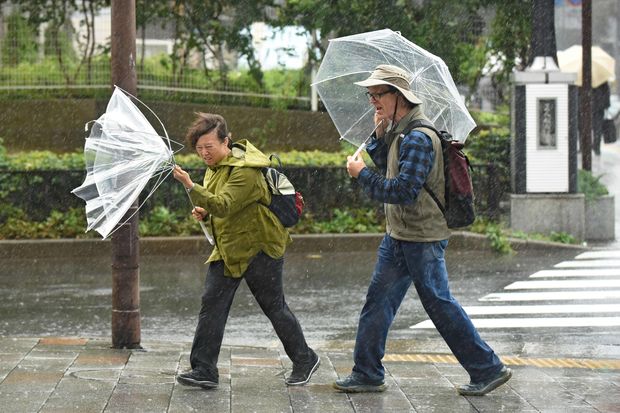 A woman have an umbrella turned inside out with strong wind in Tokyo on October 22, 2017. A powerful typhoon barrelled toward Japan on October 22, with heavy rain triggering landslides and delaying voting at one ballot station as millions struggled to the polls for a national election. / AFP PHOTO / Kazuhiro NOGI