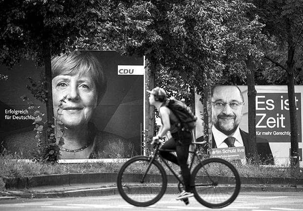 Election posters of German Chancellor Angela Merkel (CDU,L) and her main rival Martin Schulz (SPD, R) are seen as a cyclist cross Yorckstrasse in the Schoeneberg neighbourhood in Berlin on September 17, 2017. / AFP PHOTO / Odd ANDERSEN