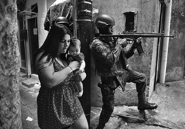 A woman walks with her baby past a PM militarized police soldier in position and aiming his rifle in Rocinha favela in Rio de Janeiro, Brazil on September 23, 2017. Although shooting was reported in the early hours of Saturday in Rocinha -- for the seventh day running -- officials said that Friday's deployment of 950 soldiers to reinforce police had brought the crisis under control. / AFP PHOTO / CARL DE SOUZA ORG XMIT: 011