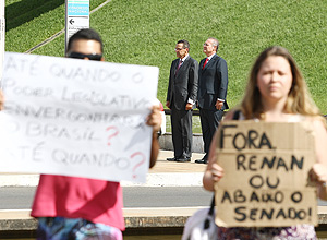 Renan Calheiros e Henrique Eduardo Alves (ao fundo) participam de cerimônia na rampa do Congresso enquanto manifestantes levantam cartazes em protesto