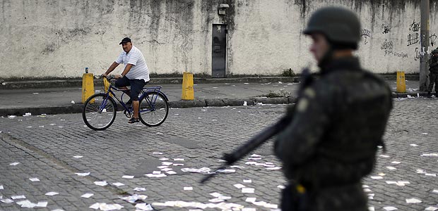 A resident cycles past a soldier standing guard during general elections in the Nova Holanda slum, inside the complexo da Mare in Rio de Janeiro, Brazil, Sunday, Oct. 5, 2014. Brazilians are casting ballots in a presidential election expected to force a three-week runoff campaign between incumbent Dilma Rousseff and one of her two top challengers, either former environment minister and senator Marina Silva or Aecio Neves. Brazilians are also deciding congressional races and electing governors. (AP Photo/Leo Correa) ORG XMIT: XLC101