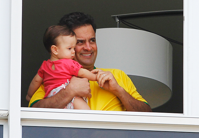 Com a camisa do Brasil, Senador Aécio Neves aparece na janela de seu apartamento na Avenida Vieira Souto em Ipanema com sua filha no colo