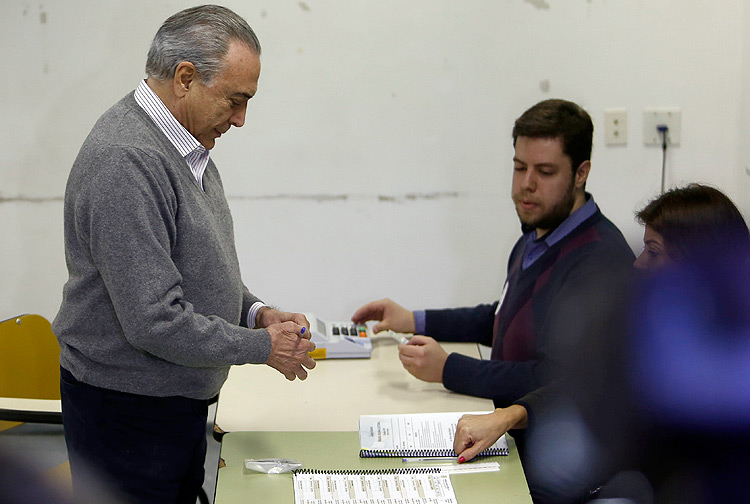 Brazilian President Michel Temer (L) votes at a polling station during municipal elections, in Sao Paulo, Brazil, on October 2, 2016. Brazilians furious at recession and corruption voted Sunday in municipal elections amid heightened security after a series of murders of candidates. Among the first to cast his ballot in the financial capital Sao Paulo was Temer from the center-left PMDB party, who took over the presidency in August after turning on his former leftist ally Dilma Rousseff and helping to force her from the top job in an impeachment vote. / AFP PHOTO / Miguel SCHINCARIOL