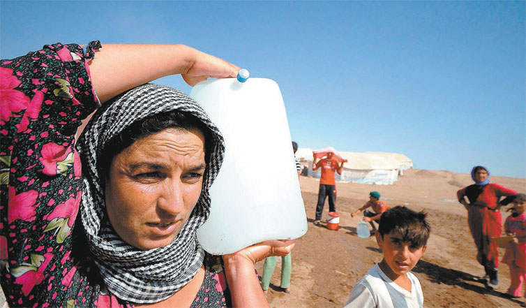 Mulher da minoria yazidi, perseguida pelo EI, carrega gua em um acampamento para refugiados em Zakho, no Iraque