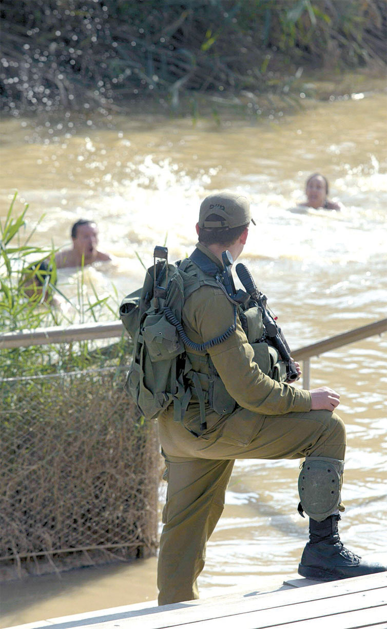 Soldado israelense faz proteo de grupo de turistas que se banham no rio Jordo