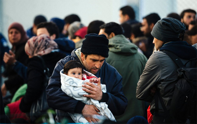 A man carries his baby as refugees wait near the border fence at the Greek-Macedonian border near the Greek village of Idomeni, on March 5, 2016, where thousands of refugees and migrants wait to cross the border into Macedonia. Some 13,000 refugees are crammed in unhygienic conditions on Greece's border with Macedonia, officials said on March 5, 2016, with all eyes on a key EU-Turkey summit on March 7 that is seen as the only viable solution to the crisis. / AFP / DIMITAR DILKOFF ORG XMIT: DIM029