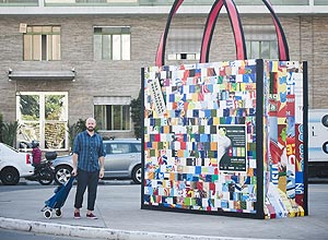 O estilista Alex Cassimiro, 33, e seu carrinho de compras, ao lado de "ecobag" gigante que fica até 16/2 na av.Paulista