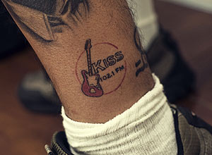 Detalhe da tatuagem do logo da Kiss FM de Denis Amorim