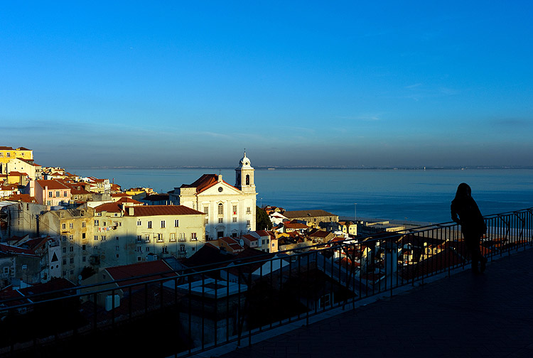 ORG XMIT: XAF101 A tourist leans against the railling of a balcony overlooking Lisbon's Alfama old neighborhood and the Tagus river at sunset Tuesday, Dec. 20 2011. (AP Photo/Armando Franca)