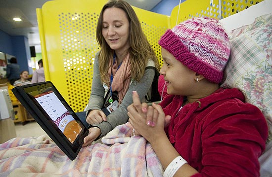 A paciente Ana Carolina Dias Muniz, 8 anos, usa um iPad com a ajuda da professora Julia Sales