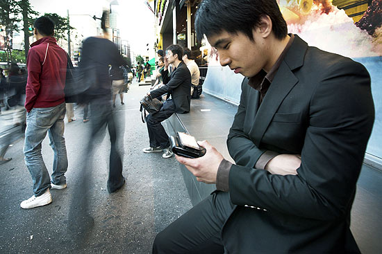 Sentado em rua de Seul, Jung Hoon assiste a programa de TV em seu celular