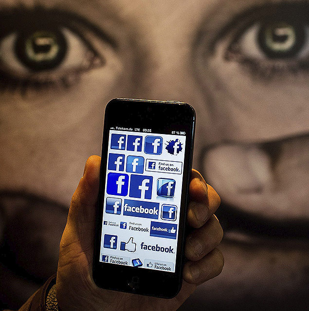 Smartphone com logotipos do Facebook  exibido em frente a um cartaz sobre "bullying" virtual durante congresso em Berlim