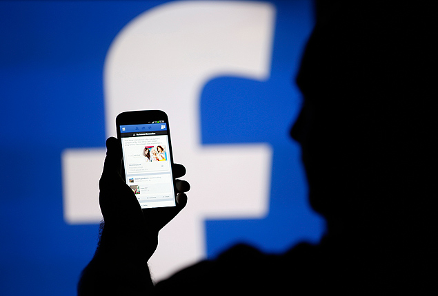 A man is silhouetted against a video screen with an Facebook logo as he poses with an Samsung smartphone in this photo illustration taken in the central Bosnian town of Zenica in a file photo taken August 14, 2013. Facebook Inc will buy fast-growing mobile-messaging startup WhatsApp for $19 billion in cash and stock, as the world's largest social network looks for ways to boost its popularity, especially among a younger crowd. REUTERS/Dado Ruvic/Files (BOSNIA AND HERZEGOVINA - Tags: BUSINESS TELECOMS) ORG XMIT: TOR903