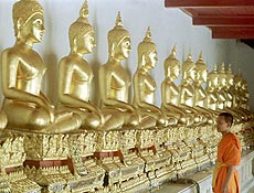 Monge budista tailands observa esttuas de ouro de Buda, em templo de Bancoc