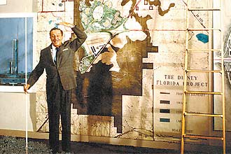 Walt Disney em frente ao mapa da Flrida, para mostrar o local do Epcot Center, inaugurado em1982; o primeiro parque da Disney na Flrida, o Magic Kingdom, abriu as portas em 1971