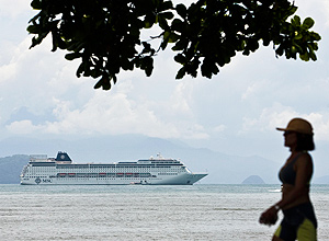 Turista passa por navio de cruzeiro próximo à orla de Ubatuba, em São Paulo