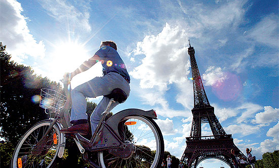Turista utiliza o sistema de empréstimo de bicicletas e circula por rua da capital francesa