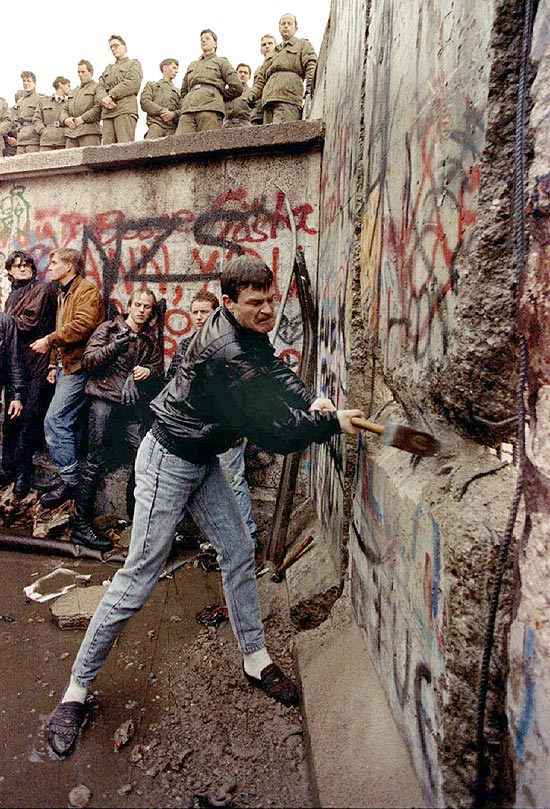 Policiais da Alemanha Oriental observam enquanto manifestante destrói pedaço do muro de Berlim