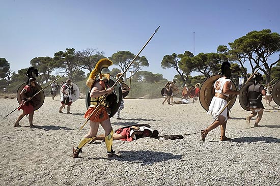 "Combatente hoplita grego ferido" no chão enquanto outros avançam para simulação da Batalha de Maratona