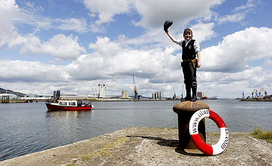 Garoto acena com chapéu diante de braço de mar em Belfast, na Irlanda do Norte; local deve se beneficiar com centenário do Titanic 