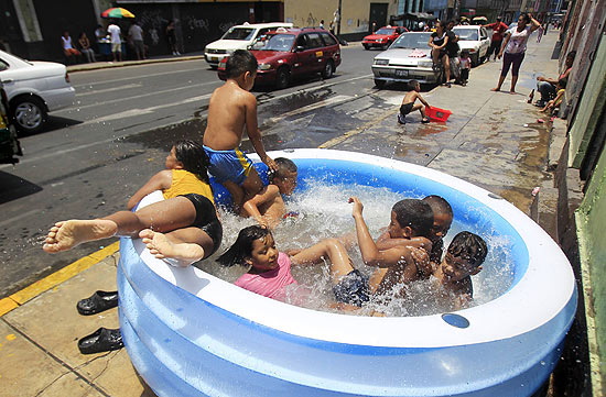 Crianças aliviam o calor brincando em piscina inflável em rua de Lima, no Peru