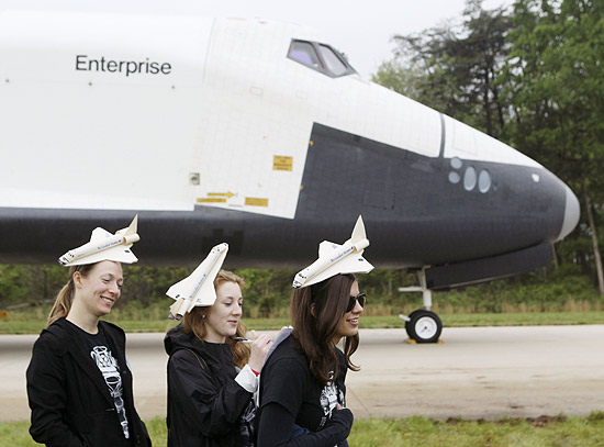 Garotas posam em frente ao ônibus espacial Discovery com chapéus no formato da nave