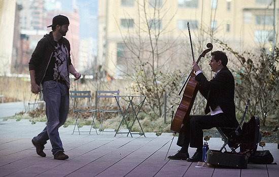Pedestre se aproxima para dar dinheiro a violinista no High Line, parque suspenso de Nova York