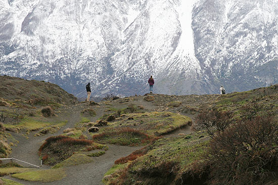 Visitantes caminham pelo parque nacional Torres del Paine, no Chile, com montanhas cobertas de neve ao fundo