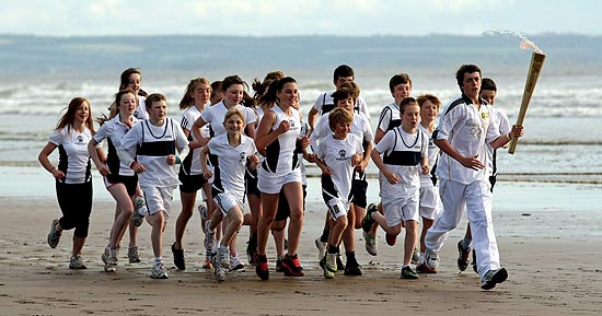 Grupo de crianas carrega tocha olmpica dos Jogos de Londres na praia de West Sands, na Esccia