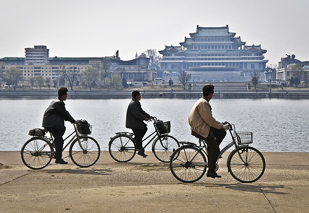 Ciclistas na margem do rio Taedong com a Grande Casa dos Estudos do Povo ao fundo, em Pyongyang 