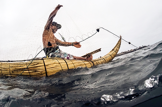 David Ucanan coleta peixes de sua rede com um barco feito de junco