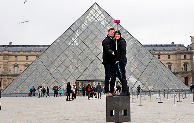 FILE - In this Tuesday, Jan. 6, 2015, Chris Baker and Jennifer Hinson from Nashville, Tennessee, use a selfie stick in front of the Louvre Pyramide in Paris. A French palace and a British museum have joined the growing list of global tourist attractions that have banned 