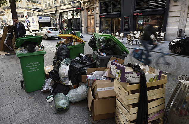 Ciclista pedala próximo a latas de lixo cheias em Paris