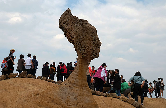 To go with "Taiwan-tourism-science-environment" by Benjamin YEH In this picture taken on October 12, 2015, tourists walk behind Taiwan's ancient "Queen's Head" rock in Yehliou, New Taipei City, in northern Taiwan. Scientists are battling to save Taiwan's ancient "Queen's Head" rock from erosion -- but the island is split over whether technology should be used to preserve the precarious natural masterpiece. More than three million people visit the coastal landmark in northern Yehliu each year, named for its supposed likeness to England's Queen Elizabeth I. AFP PHOTO / Sam Yeh ORG XMIT: SY2236