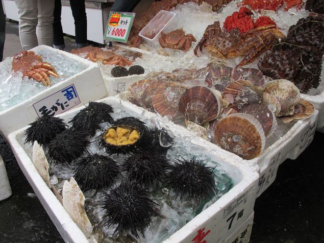 Ourio-do-mar (de cor preta) e outras iguarias  venda no mercado matinal de Hakodate
