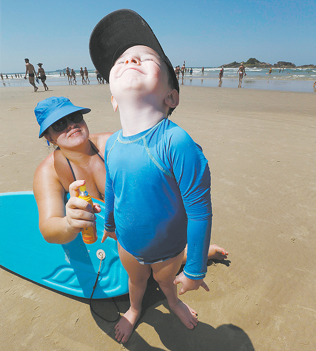Renata Pupo Silveira passa repelente no filho Enzo, 4, em praia do Guaruj