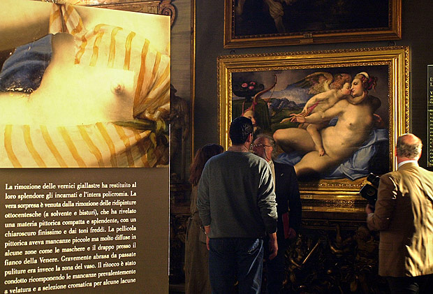 ORG XMIT: 125701_1.tif Antes e depois da pintura restaurada "Vnus e o Cupido" de Michele di Ridolfo del Ghirlandaio em exposio em Roma, Itlia. Journalists look at the newly restored painting "Venus and Cupid", right, by Italian Mannerist Michele di Ridolfo del Ghirlandaio (1483-1561) on display at Rome's Galleria Colonna during a preview for the media, Thursday, March 22, 2001. Along with centuries of grime, restorers have stripped the robes from the painting by the 16th century Mannerist, leaving a voluptuous Venus for gallery-goers to admire. At left, a poster explaining how the painting was brought back to its original beauty before the striped gown and blue cloth covering a nude woman were added for modesty in the early 19th century. (AP Photo/Massimo Sambucetti) 
