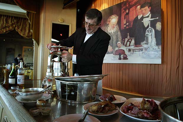 ORG XMIT: 144301_1.tif O chef Jean-Pierre Marchand em seu restaurante "La Tour d'Argent", em Paris, visitado por "gastronautas", que dedicam suas viagens  gastronomia. "LA TOUR D'ARGENT CELEBRE SON MILLIONIEME CANARD ET INTR`NISE SON FUTUR PATRON". Le "canardier" du restaurant "La Tour d'Argent", Jean-Pierre Marchand prpare un canard au sang, l'une des spcialits de l'tablissement, le 18 avril 2003  Paris, devant un tableau reprsentant l'ancien propritaire des lieux, Frdric Delair, numrotant son premier canard au sang en 1890. Claude Terrail, 85 ans, le propritaire de "La Tour d'Argent", restaurant connu dans le monde entier, ftera le 29 avril prochain, en prsence de 140 personnalits le sacrifice du millionime canard. Claude Terrail en profitera pour introniser son fils de 22 ans,  qui il a donn le prnom de son pre Andr. AFP PHOTO DANIEL JANIN 