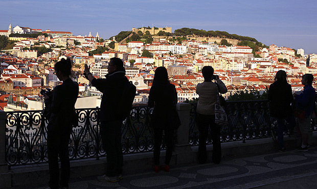 In this May 25, 2016 photo, tourists taking pictures are silhouetted against Lisbon's old center lit by the setting sun. With sunny days getting longer and lazier, sparkling beaches warming up and terrorism fears driving customers away from other Mediterranean destinations, Spain and Portugal are reaping an economic bonanza from tourism. (AP Photo/Armando Franca) ORG XMIT: EM102