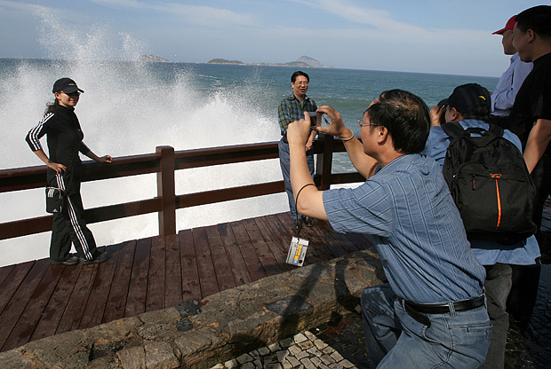 Grupo de turistas chineses tira fotos da ressaca na praia do Leblon, no Rio