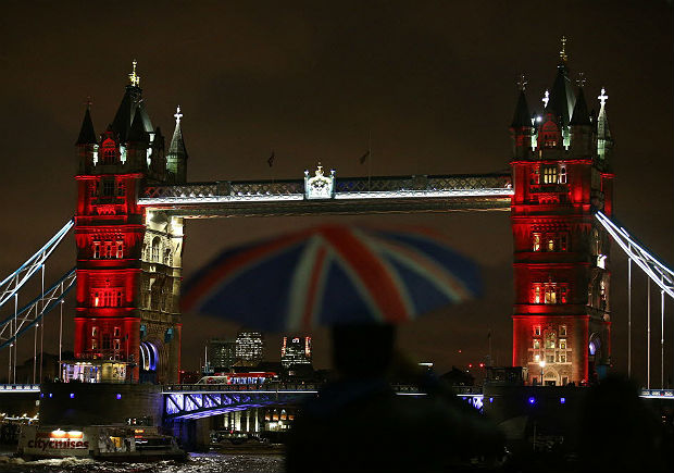 Homem com guarda-chuva com a bandeira do Reino Unido passa pela Tower Bridge