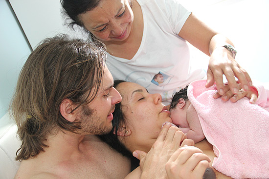 Katia ao lado do marido Ayrton e da mãe Cleusa minutos após o nascimento de Sara, na cama do casal 
