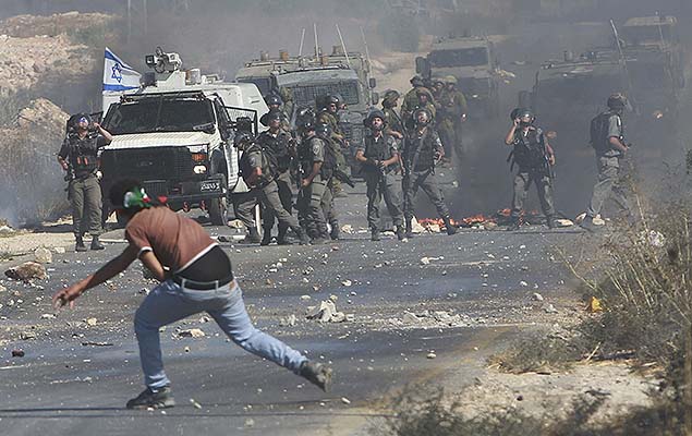 Um protestante palestino joga pedras em militares israelenses, em agosto