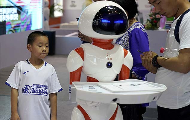 Criança observa um robô humanoide durante a feira China Robot Show, que acontece de 5 a 8 de julho em Xangai