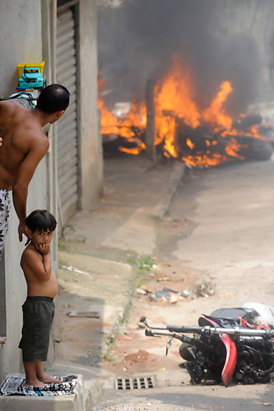 Homem e criança observam veículo incendiado Leia Mais