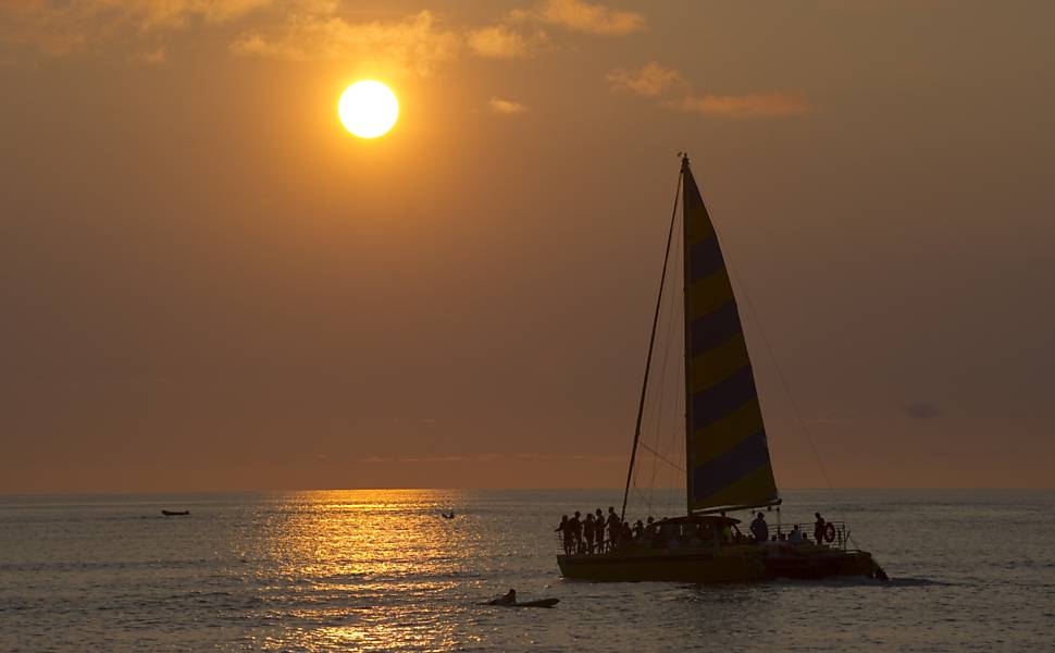 Barco a vela leva turistas para excursão ao longo da praia de Waikiki, durante o pôr-do-sol em Honolulu, Havaí, na véspera de Natal; praia, na costa sul da ilha de Oahu, é destino turístico popular desde o século 19